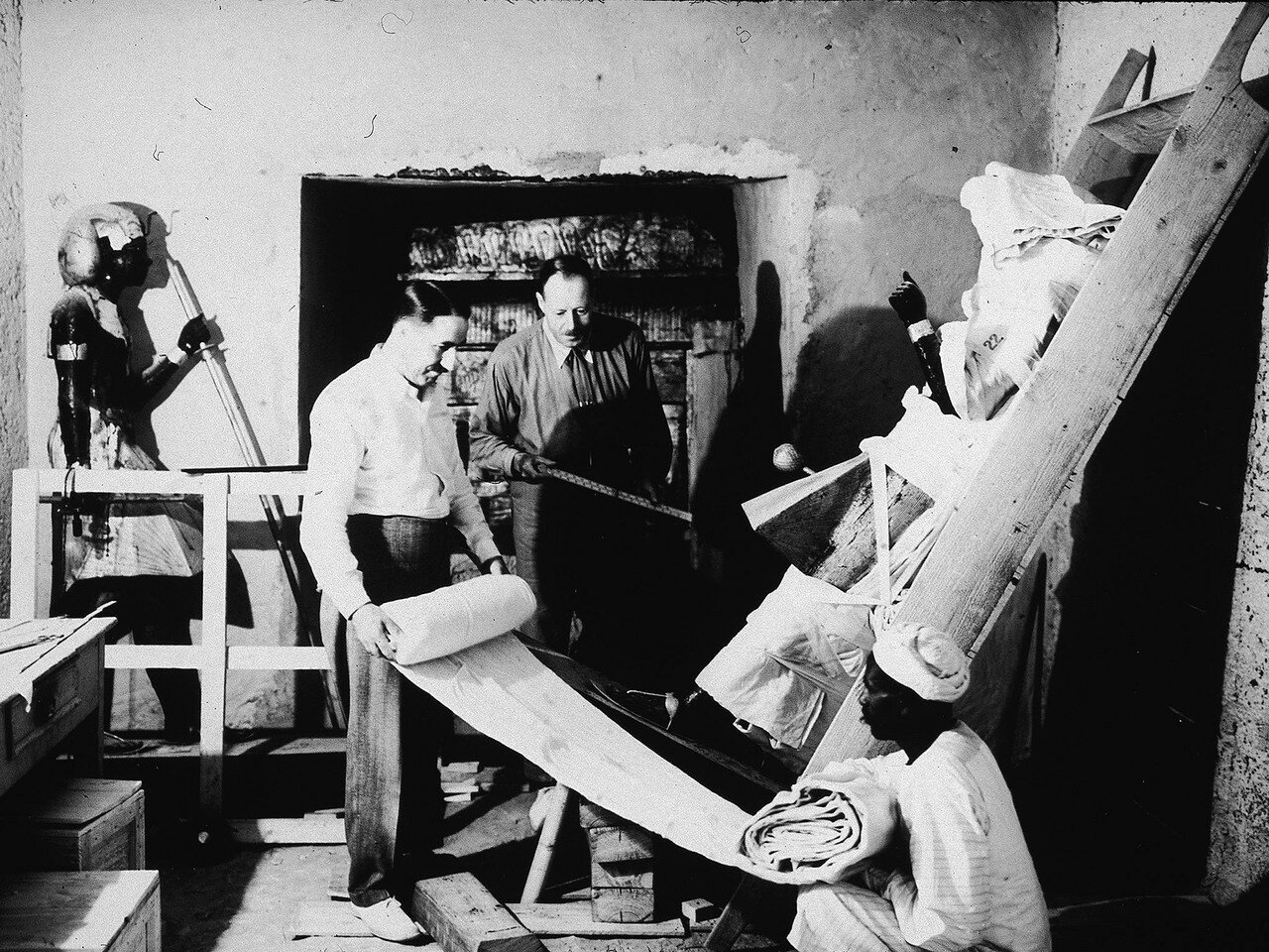 Британские археологи Говард Картер (слева) и Артур Каллендер извлекают предметы из гробницы фараона Тутанхамона с помощью египетского рабочего. 1923